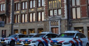 Nederlandse politieauto's geparkeerd voor een historisch gebouw met sierlijke architectuur, overdag.